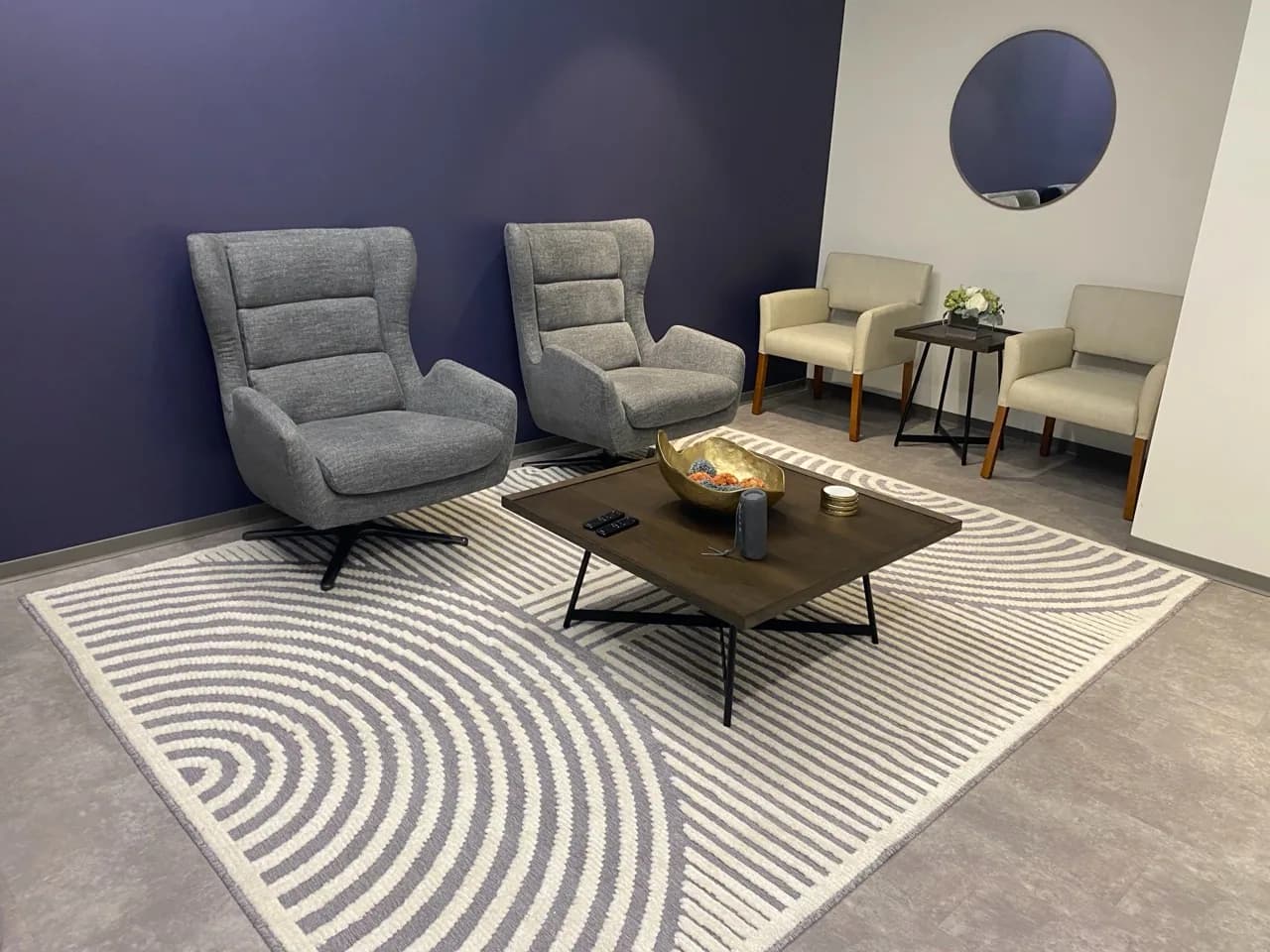 A completed lounge arrangement with two gray swivel chairs, two guest chairs, a coffee table, a side table, and a large area rug.