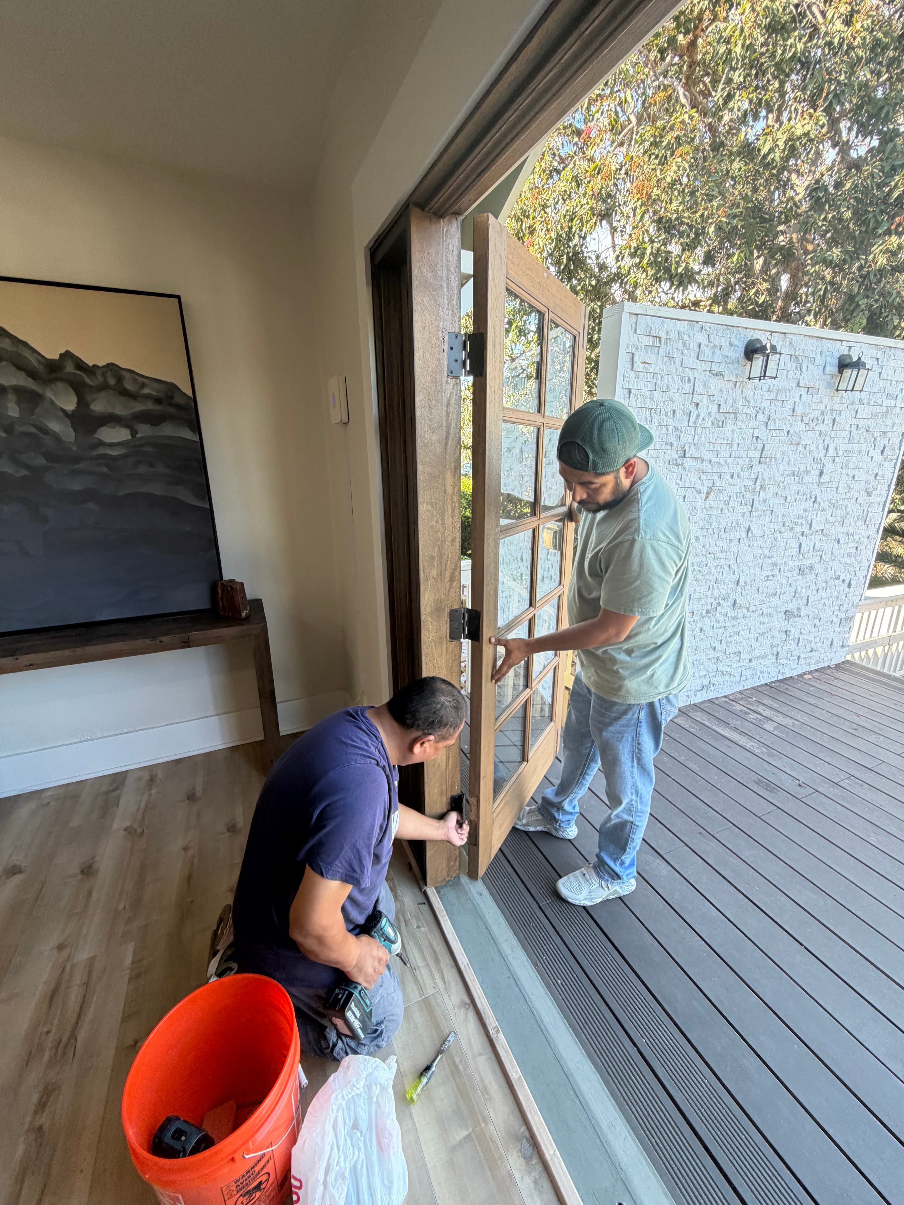 Two installers carefully aligning a wood-framed exterior door during a repair and refit project.