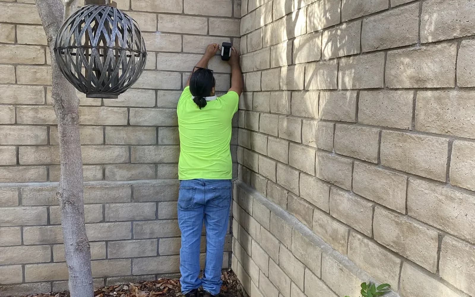 An installer positioning a compact outdoor camera on a masonry wall.