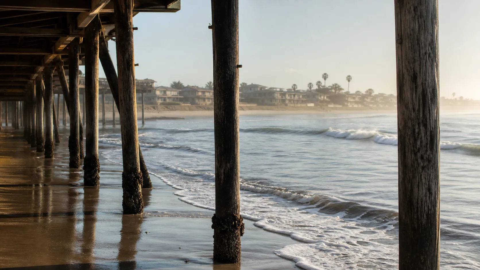 Illustrative view through weathered pier pilings and surf, inspired by Pacific Beach's Crystal Pier.